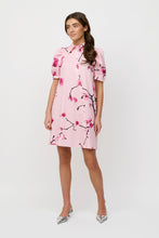 Load image into Gallery viewer, CRETON La shirt dress with an elegant and spring-inspired look. Style it simply with flat sandals for everyday wear or with pointed heels for a more refined look.

Short shirt dress with a straight, loose silhouette
Short puff sleeves with small cuffs
Classic shirt collar
Asymmetrical, full-length button closure
Discreet side pockets
Slightly rounded bottom
Japanese cherry tree print

70% cotton, 27% nylon, 3% elastane