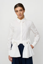 Load image into Gallery viewer, Chin Shirt from Créton

Details

Classic shirt collar and hidden button closure
Decorative bows at the waist as an integral part of the design
Slightly cropped length with volume at the hip
Long sleeves with cuffs
Smooth and light structure with an elegant look

Styling
A modern shirt with a feminine twist. The distinctive bows add a playful and stylish expression that elevates an otherwise classic design. Style it with wide trousers for a trendy look, or combine with a skirt for a more elegant and feminine