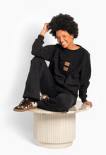 Load image into Gallery viewer, A refined take on the classic college sweatshirt, crafted in a soft cotton-blend jersey with a relaxed silhouette and raglan sleeves. The signature Hést emblem is elevated through a textured appliqué and tonal embroidery, creating a subtle statement against the dark base. Finished with ribbed trims for a clean, sporty look that transitions effortlessly from everyday wear to elevated casual styling.