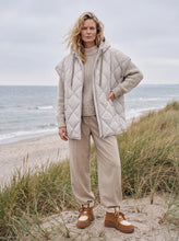 Load image into Gallery viewer, A padded cape with a generous silhouette and thermal filling, for cool autumn days.


This padded cape has a generous silhouette with a thermal filling that offers warmth while keeping a supple, versatile feel. Push buttons along the side seams allow for an adjustable fit, while a fixed hood and fleece-lined welt pockets with decorative stitching add both function and detail. A two-way YKK zipper at the front completes the design. Perfect for cool autumn days.