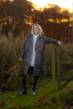 Load image into Gallery viewer, This long winter coat is made from a waxed cotton fabric with a quilted lining and fleece-lined welt side pockets. It features flap pockets and side slits with push button closures. The centre front has a two-way zipper concealed beneath a protective placket. It is finished with a detachable, adjustable hood and cuff straps.

Materials:

Composition: 65% Cotton, 35% Polyester
Lining: 100% Polyester
Padding: 100% Polyester