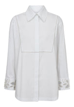 Load image into Gallery viewer, Dahlia Long Shirt is a contemporary update to the crisp white shirt. Designed with a decorative front flap detail and delicate embellishment along the cuffs and shoulders, it blends tailoring tradition with modern femininity.
The slightly A-line silhouette ensures an effortless fit, while the clean lines and hidden placket add a minimalist finish.
Size &amp; Fit
• Regular fit
• Slightly A-line shape
• Hip length
• Long sleeves
Details
• Classic cotton shirt with elevated details
