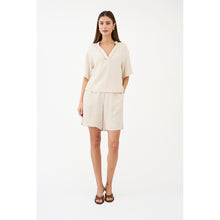 Load image into Gallery viewer, The Miles Blouse is a refined essential with a relaxed, modern feel. Crafted in a softly textured oyster white melange, it features a clean silhouette with a subtle V-neckline accented by delicate trim detailing.
Size &amp; Fit
• Relaxed fit
• Straight silhouette
• Slightly cropped length
• Short, wide sleeves
Details
• V-neckline with subtle trim detail
• Lightweight and breathable