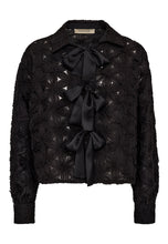 Load image into Gallery viewer, he Lexie 3D Chiffon Tie Shirt is a bold statement in texture and femininity. Featuring sculptural chiffon flowers and three oversized satin bows, this sheer button-up reimagines romantic tailoring with a graphic edge.
The crisp collar and tailored cuffs provide contrast to the playful silhouette, making it a standout choice for both day-to-night dressing and elevated layering.
Size &amp; Fit
• True to size
• Straight fit
• Cropped length
Details
• Semi-sheer chiffon with 3D floral texture
